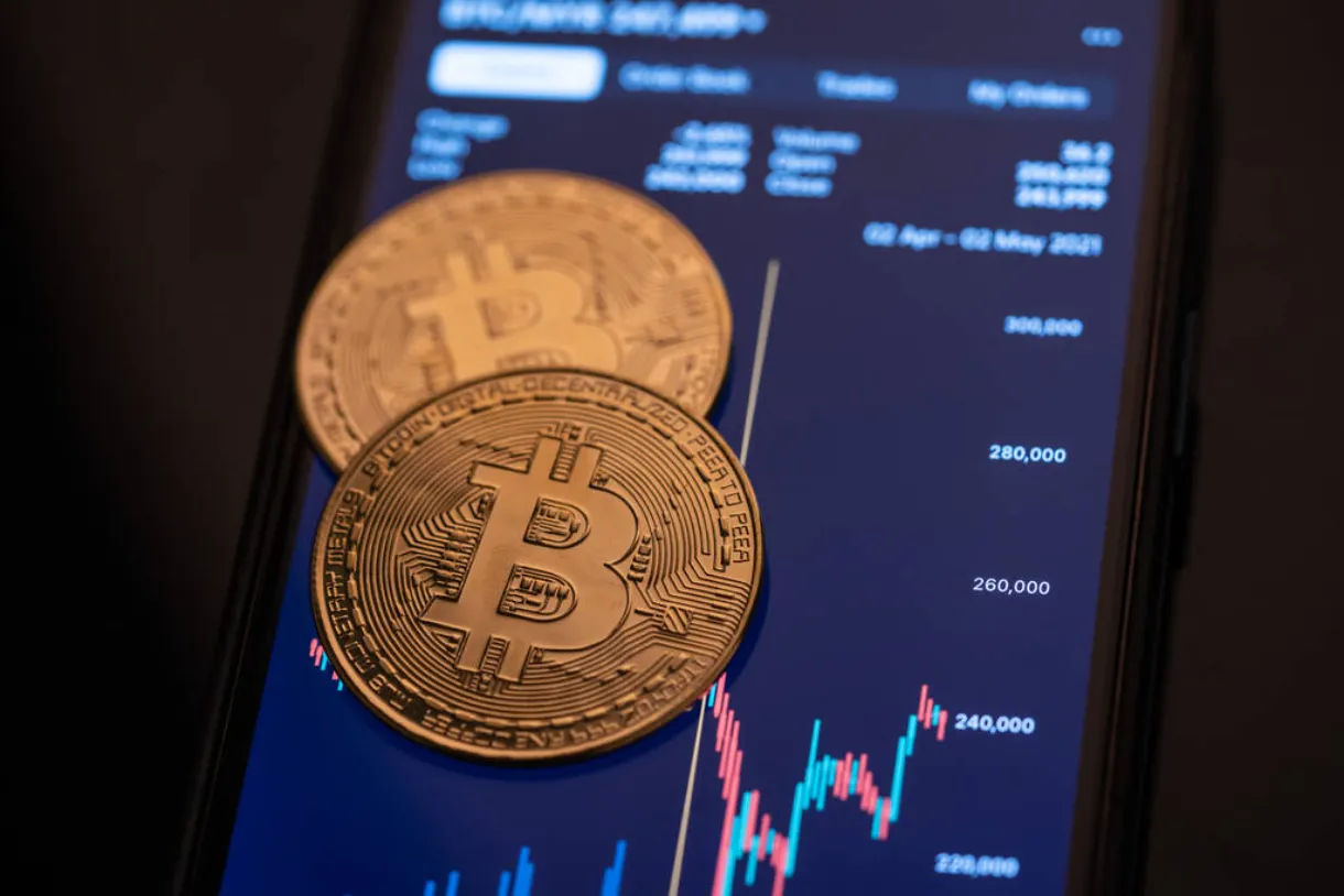 Two bitcoin coins are on the screen of a trading chart via the smartphone.